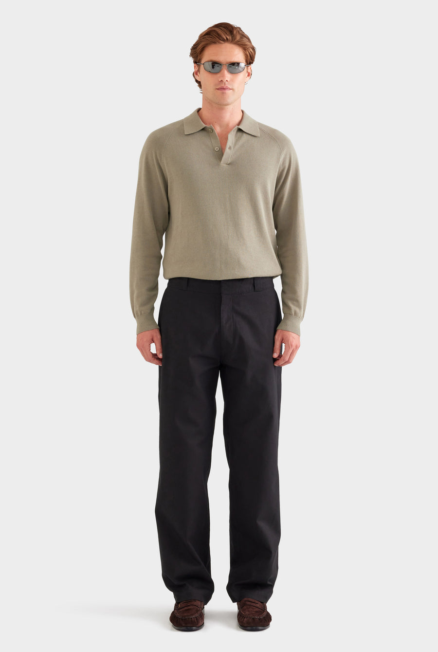 Man wearing a beige long-sleeve polo shirt and black pants on a white background