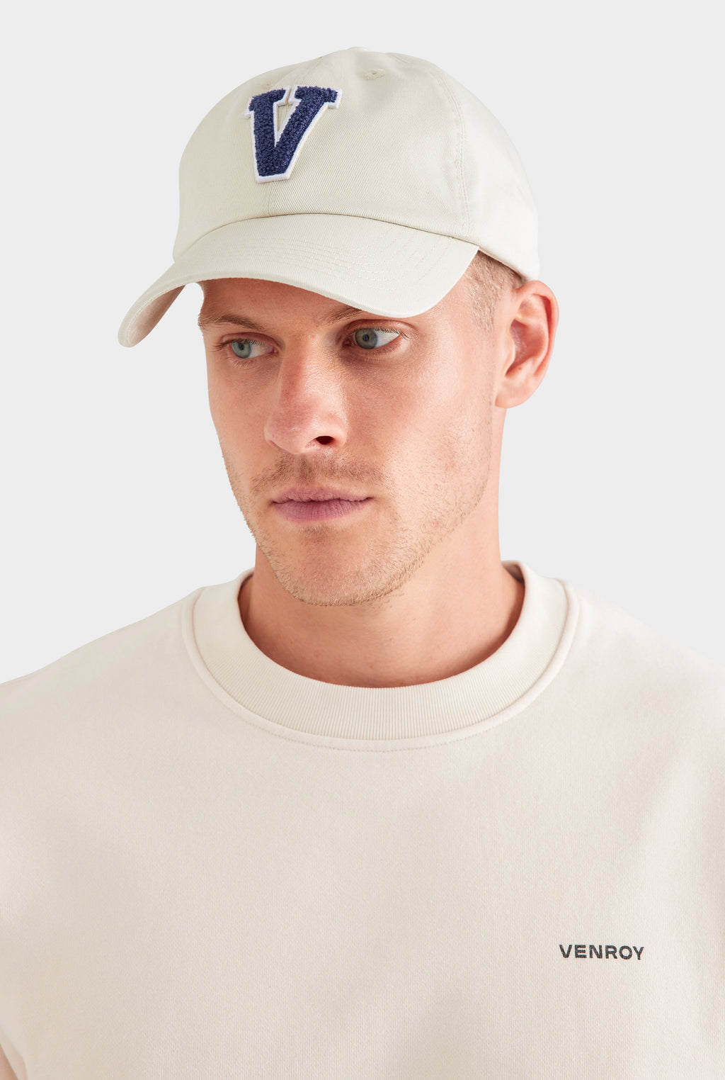 Man wearing a beige cap with a blue 'V' logo on a white background