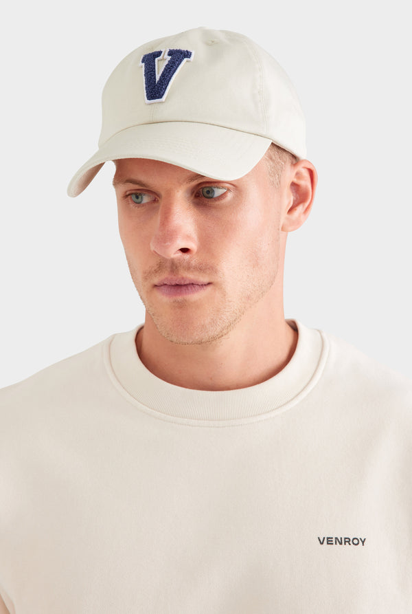 Man wearing a beige cap with a blue 'V' logo on a white background