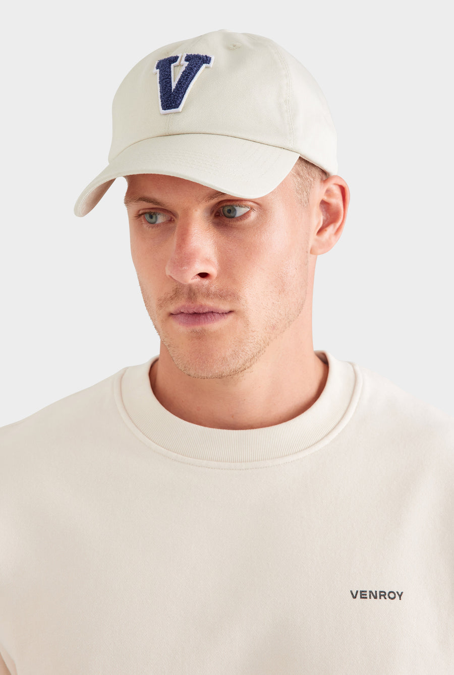 Man wearing a beige cap with a blue 'V' logo on a white background