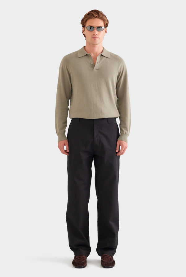 Man wearing a beige long-sleeve polo shirt and black pants on a white background